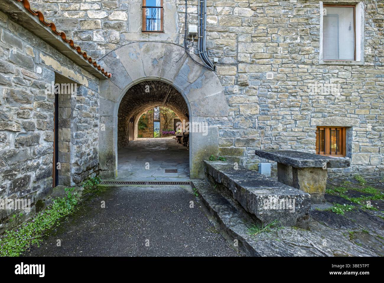 Tunnel ad arco in pietra In Un villaggio storico, che conduce a Un'uscita luminosa. Architettura tradizionale, fascino rurale, vista panoramica, muri a trama Foto Stock