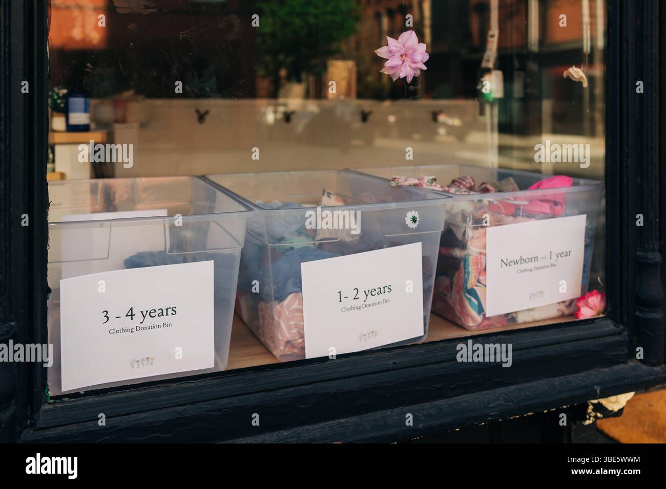 I contenitori di donazione trasparenti etichettati per fascia d'età aiutano a raccogliere vestiti per i bambini bisognosi, promuovendo il sostegno della comunità. Foto Stock