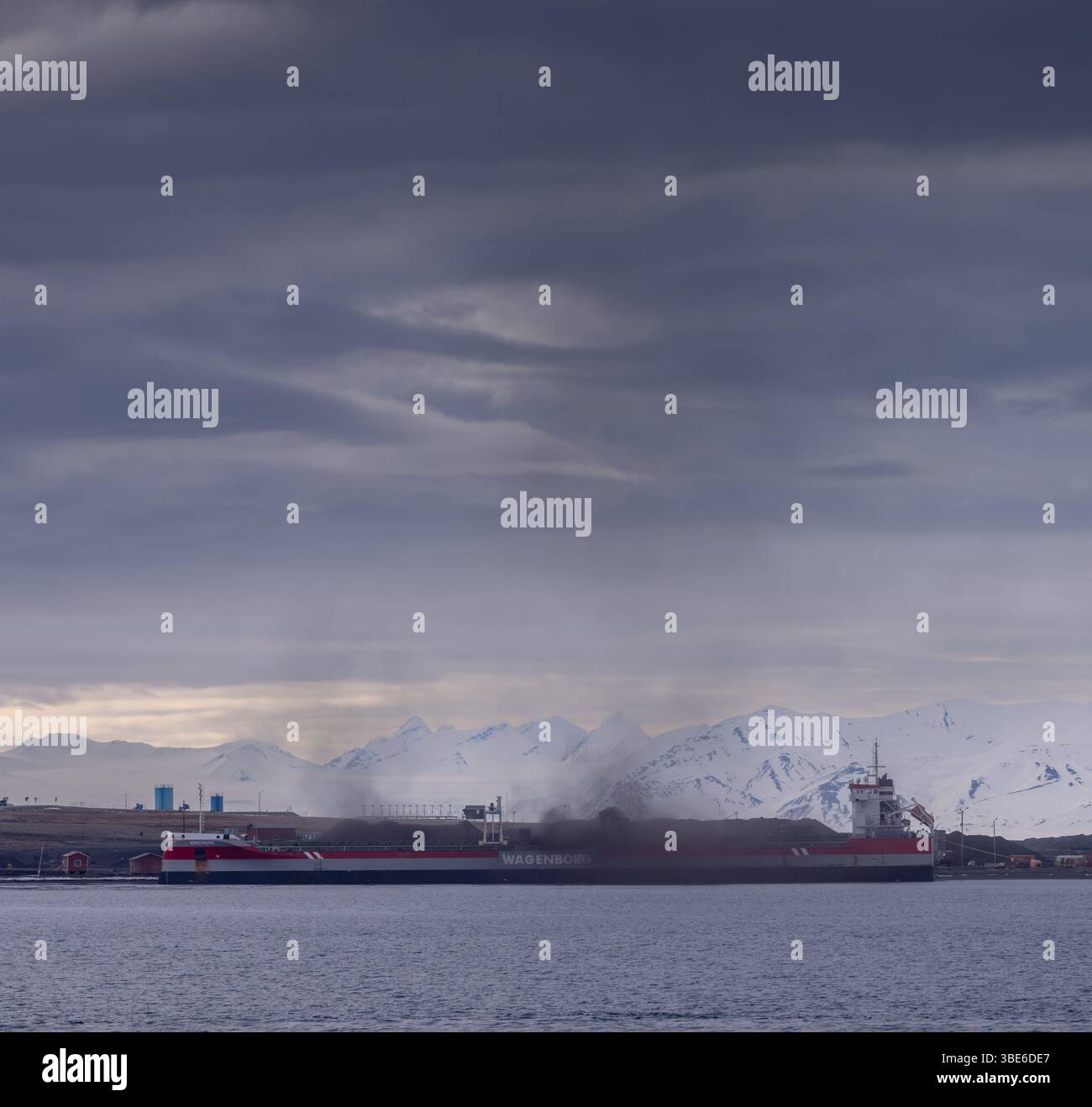 La nave di Wagenborg rilascia un pennacchio di polvere di carbone durante le operazioni di carico alle Svalbard, in Norvegia, sotto nuvole umide e montagne innevate. Foto Stock