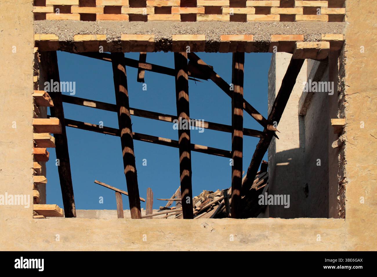 Primo piano di una finestra frantumata in un muro di una fattoria in rovina, aperta agli elementi e al passare del tempo. Travi in legno crollate che ricordano una vita passata. Foto Stock