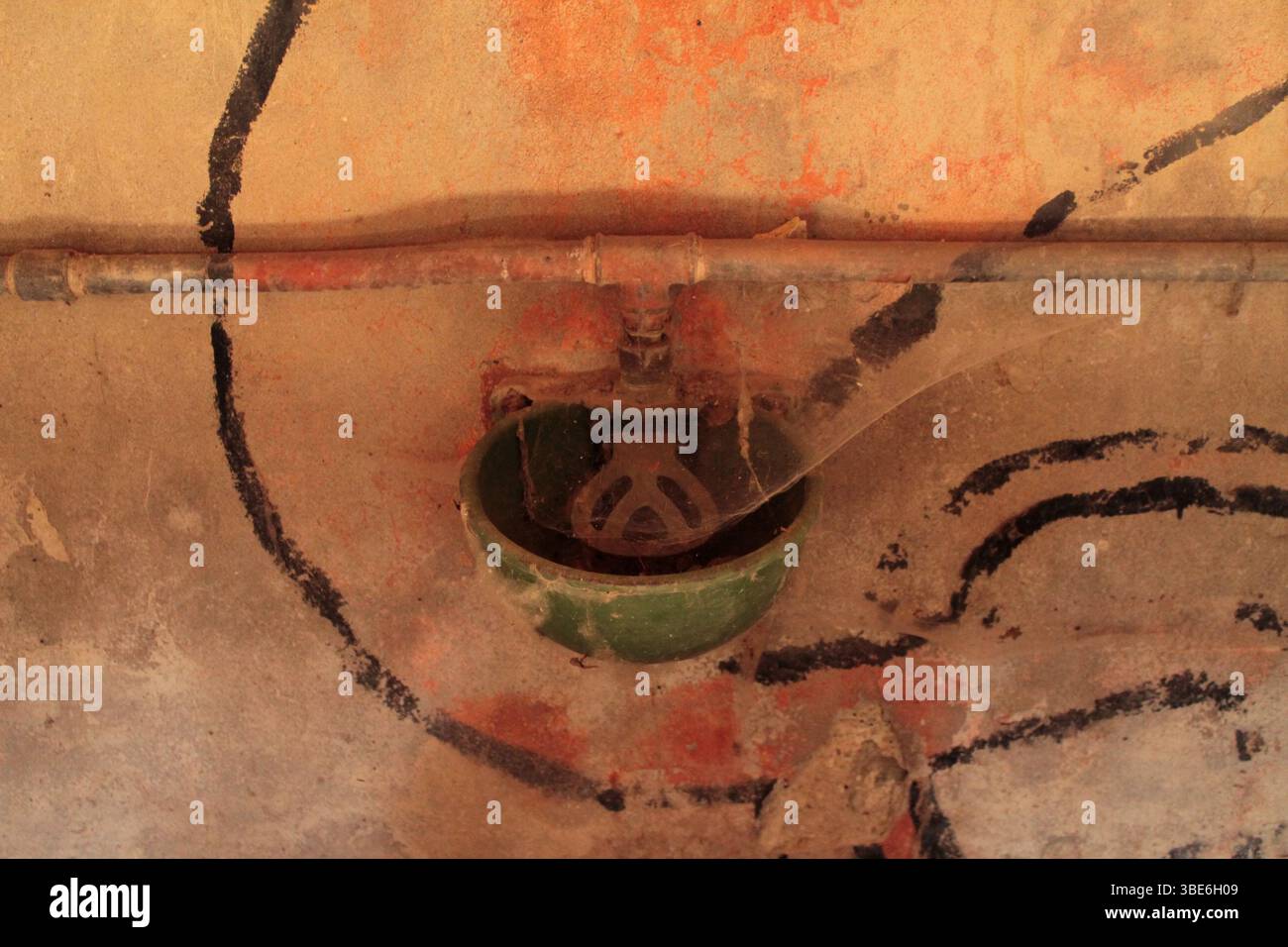 Un vecchio alimentatore in una casa colonica abbandonata, piena di ragnatele, circondata da scritti sul muro, per ricordarci il costante passare del tempo. Foto Stock