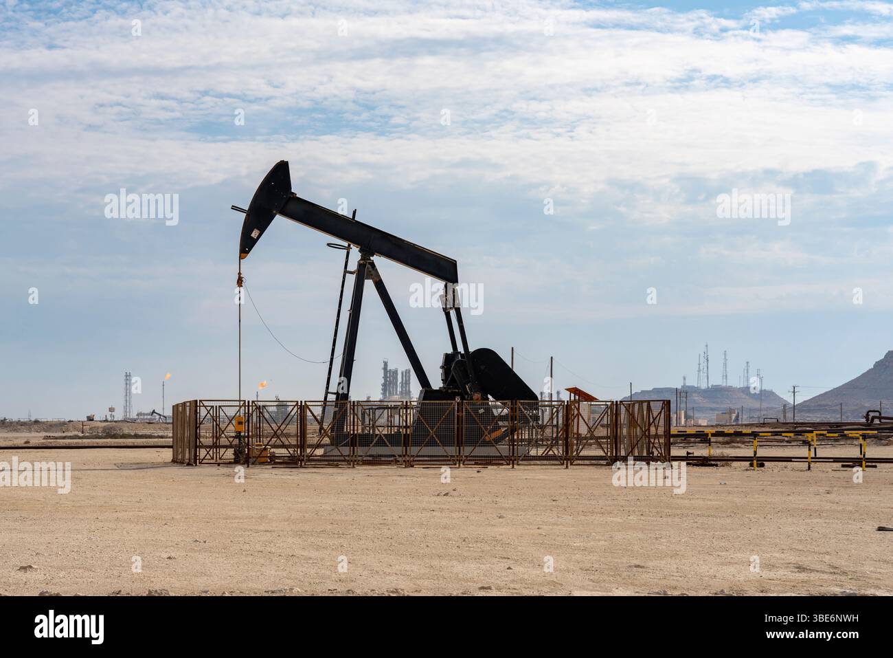 Il martinetto a pompa dell'olio opera nel paesaggio desertico del Bahrein sotto un cielo nuvoloso che rappresenta l'industria petrolifera e la produzione di energia del paese. Foto Stock