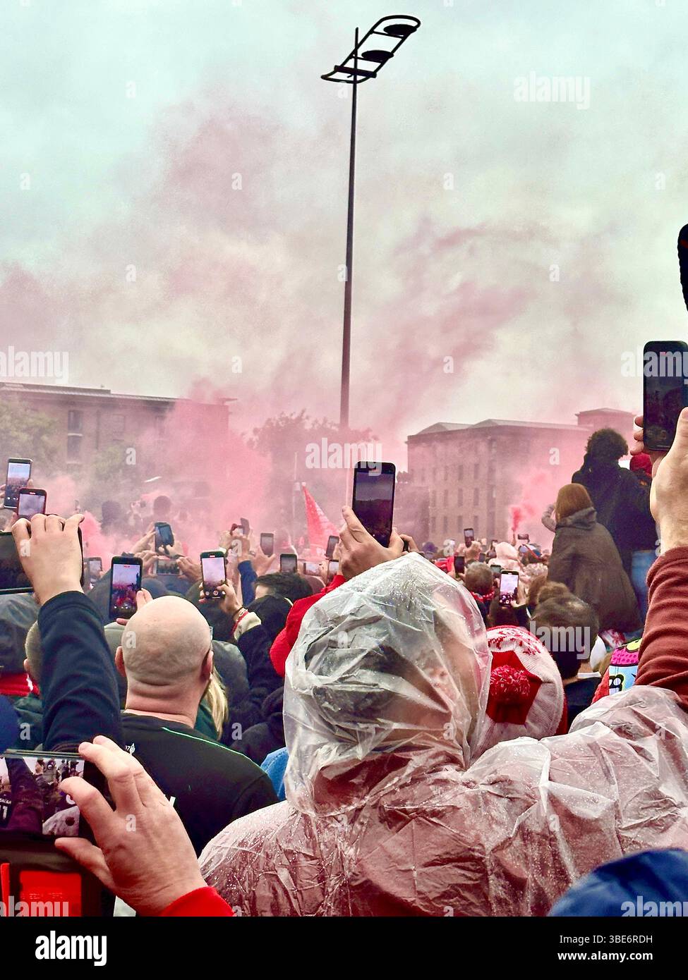 I fan girano la parata del Liverpool FC mentre la folla si riunisce a Strand Street, Liverpool, Regno Unito, prima dell'arrivo dell'autobus scoperto della squadra. 26 maggio 2025. - Immagine stock catturata con smartphone