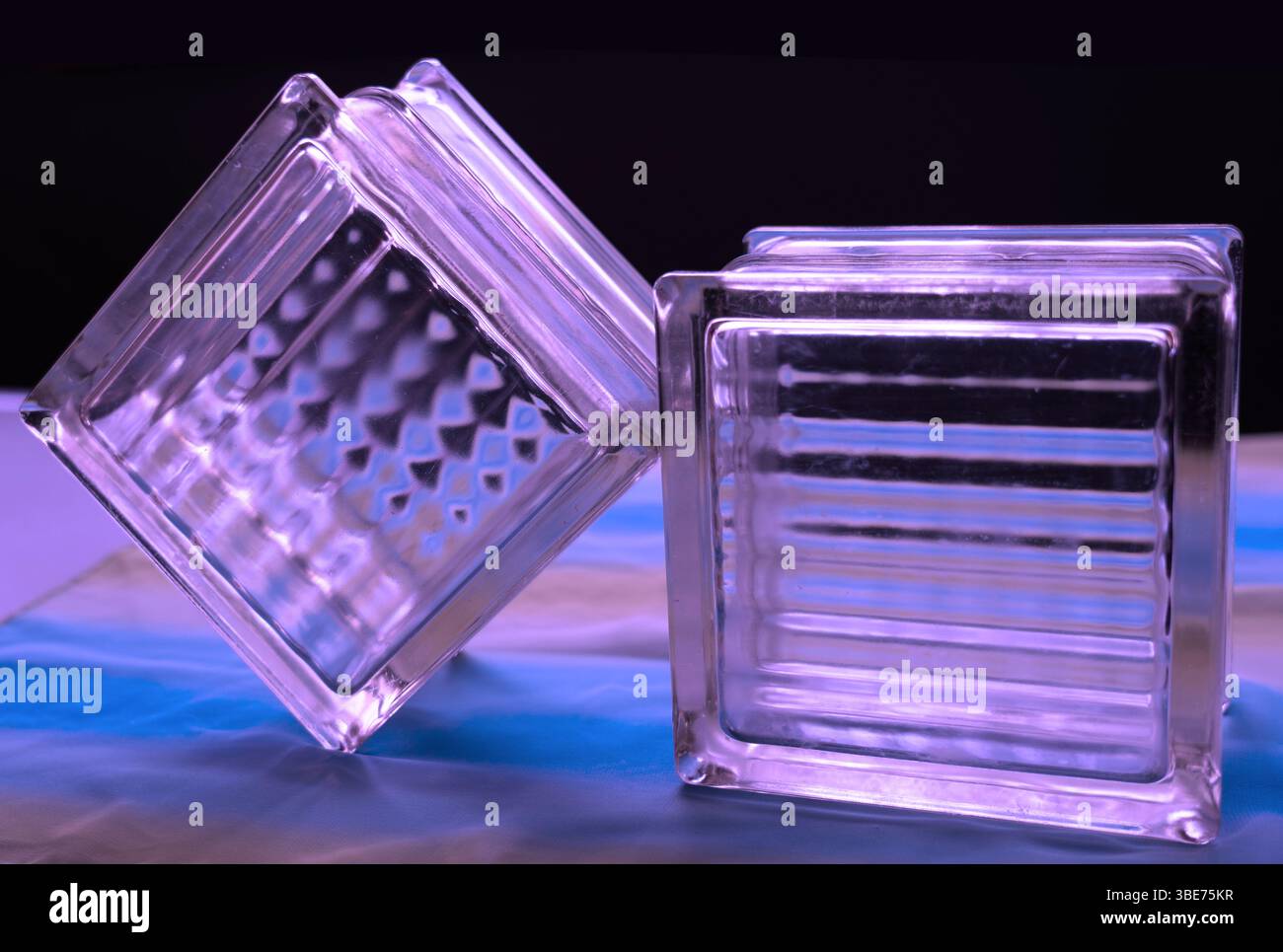 La rifrazione leggera sui blocchi di vetro riflette le forme delle linee di diamante in blu e verde. Cubi inclinabili per la visualizzazione in primo piano con sfondo nero. Foto Stock