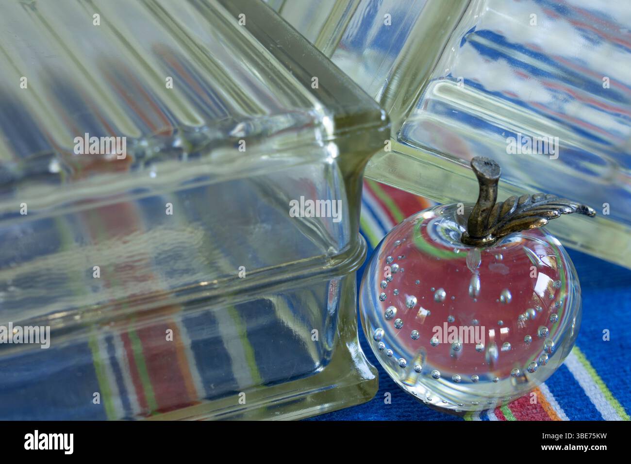 La mela di vetro visualizzata con rifrazione leggera sui blocchi di vetro mostra i colori del panno a strisce sottostante. I blocchi per finestre trasparenti hanno un design a nervatura. Foto Stock