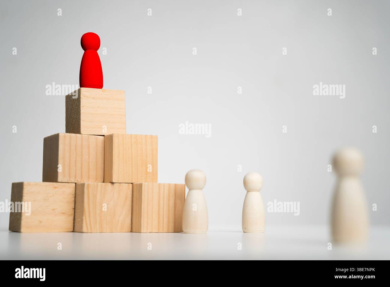 Una figura rossa di legno si erge in cima a una piramide fatta di blocchi di legno, che simboleggia leadership, gerarchia, successo, visione, e autorita' con memb di squadra Foto Stock