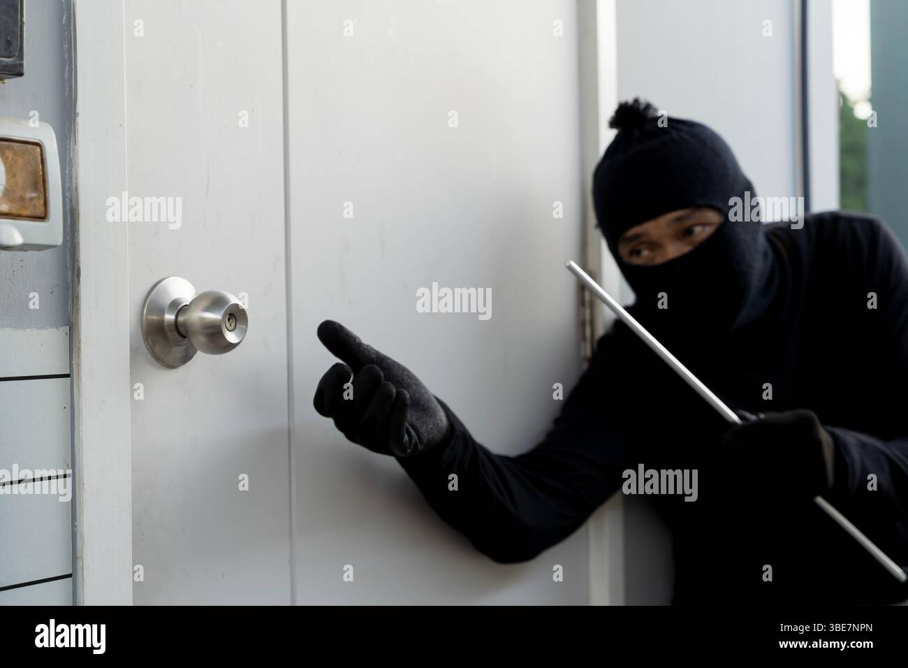 Ladro mascherato in abito nero che tiene un palanchino mentre cerca di entrare in una casa. Concetto di furto, invasione domestica, rischio di sicurezza e proprietà c Foto Stock Ladro mascherato in abito nero che tiene un palanchino mentre cerca di entrare in una casa. Concetto di furto, invasione domestica, rischio di sicurezza e proprietà c Foto Stock
