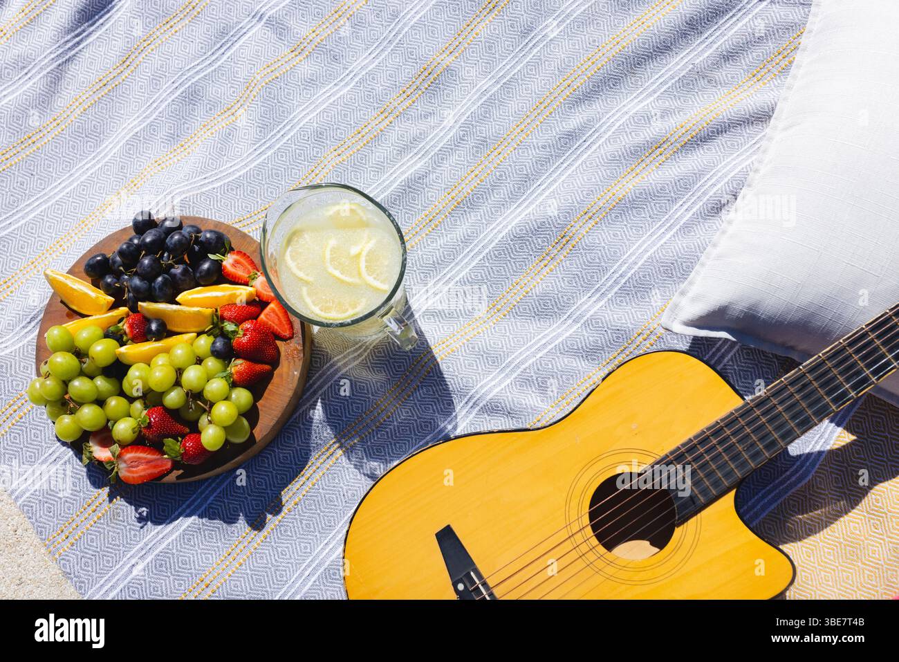 Vassoio di frutta in legno appoggiato su una coperta a righe sulla sabbia, con limonata, frutta e chitarra Foto Stock