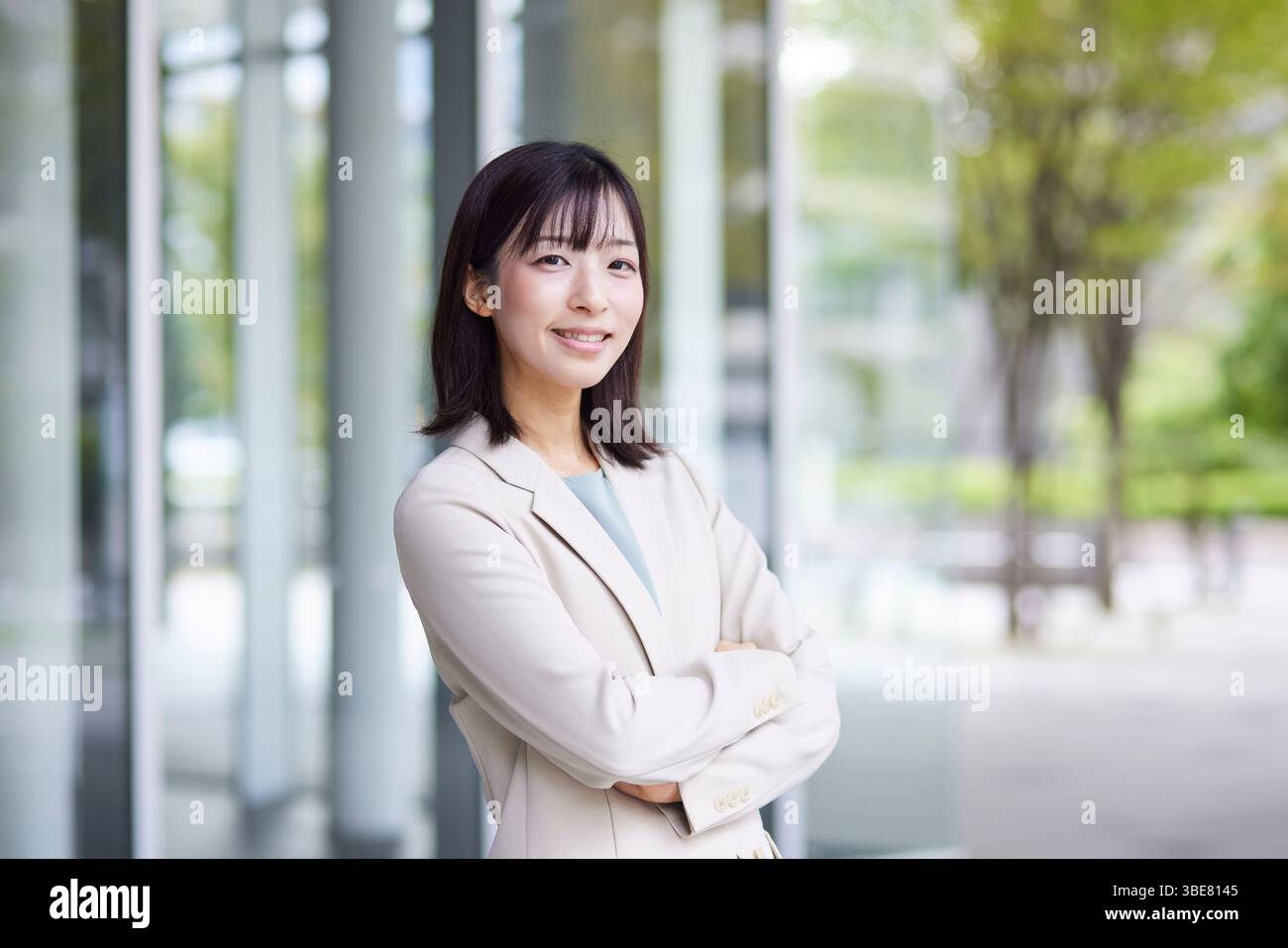 Donna giapponese sorridente in tuta con le braccia piegate di fronte all'ufficio Foto Stock