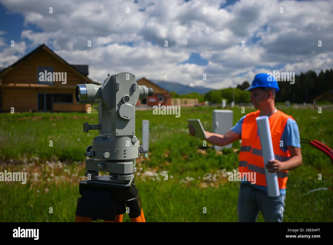 Surveyor che lavora con teodolite e tablet durante la topografia per la costruzione di nuove abitazioni. Foto Stock