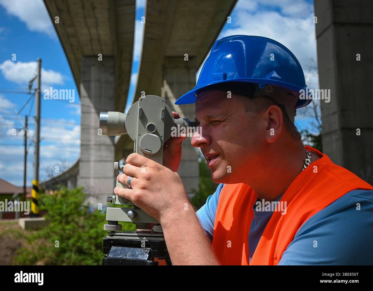 Surveyor che lavora con il livello di transito teodolite durante la costruzione del cavalcavia autostradale. Foto Stock