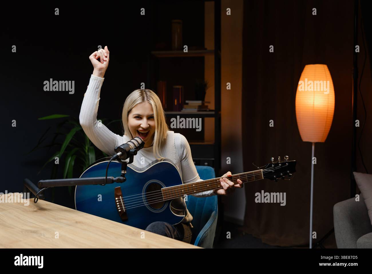 Musicista donna che registra una canzone suonando la chitarra acustica e cantando durante il concerto live streaming online Foto Stock