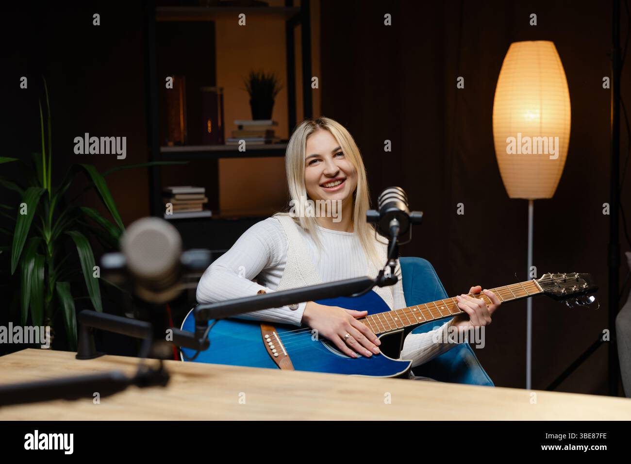 Musicista sorridente che canta e suona la chitarra acustica mentre registra una canzone in uno studio domestico Foto Stock