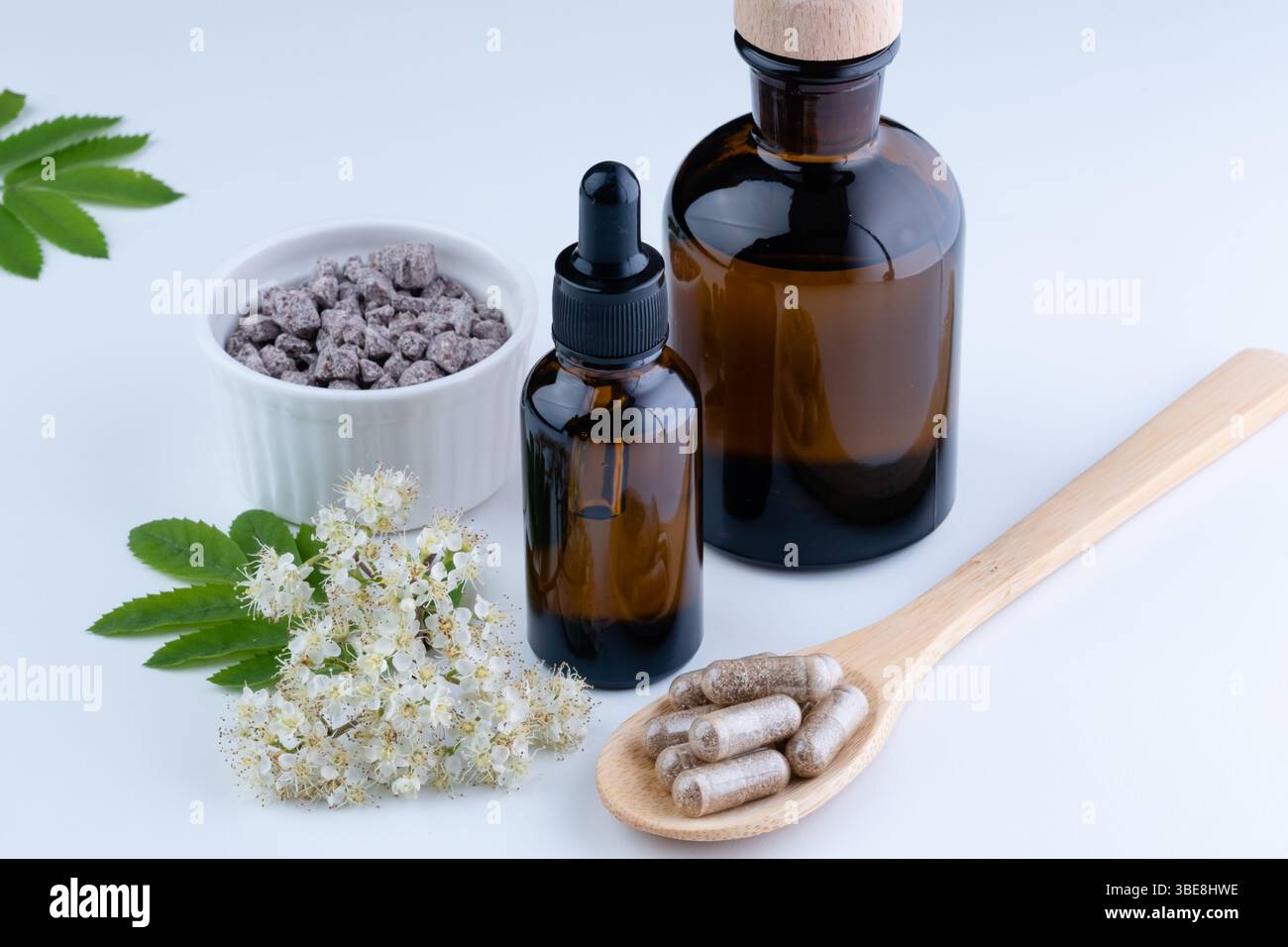 Integratori a base di erbe e mockup di flacone contagocce in vetro soffiato su un cucchiaio di legno con fiore di sambuco in fiore su sfondo bianco. Foto Stock