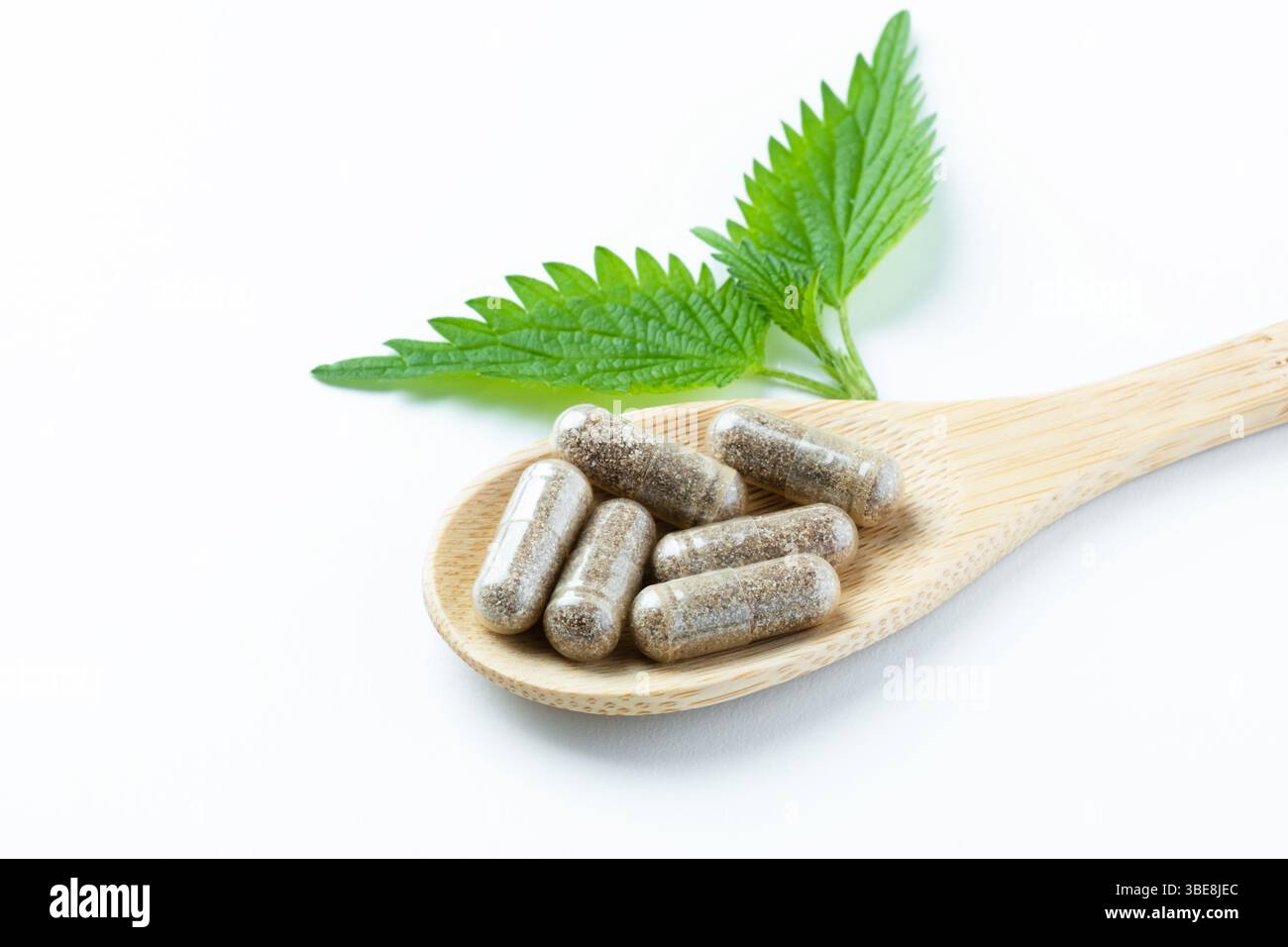Integratori a base di erbe su un cucchiaio di legno con ortica su sfondo bianco. Medicina alternativa, concetto di tema sano e benessere. Foto Stock