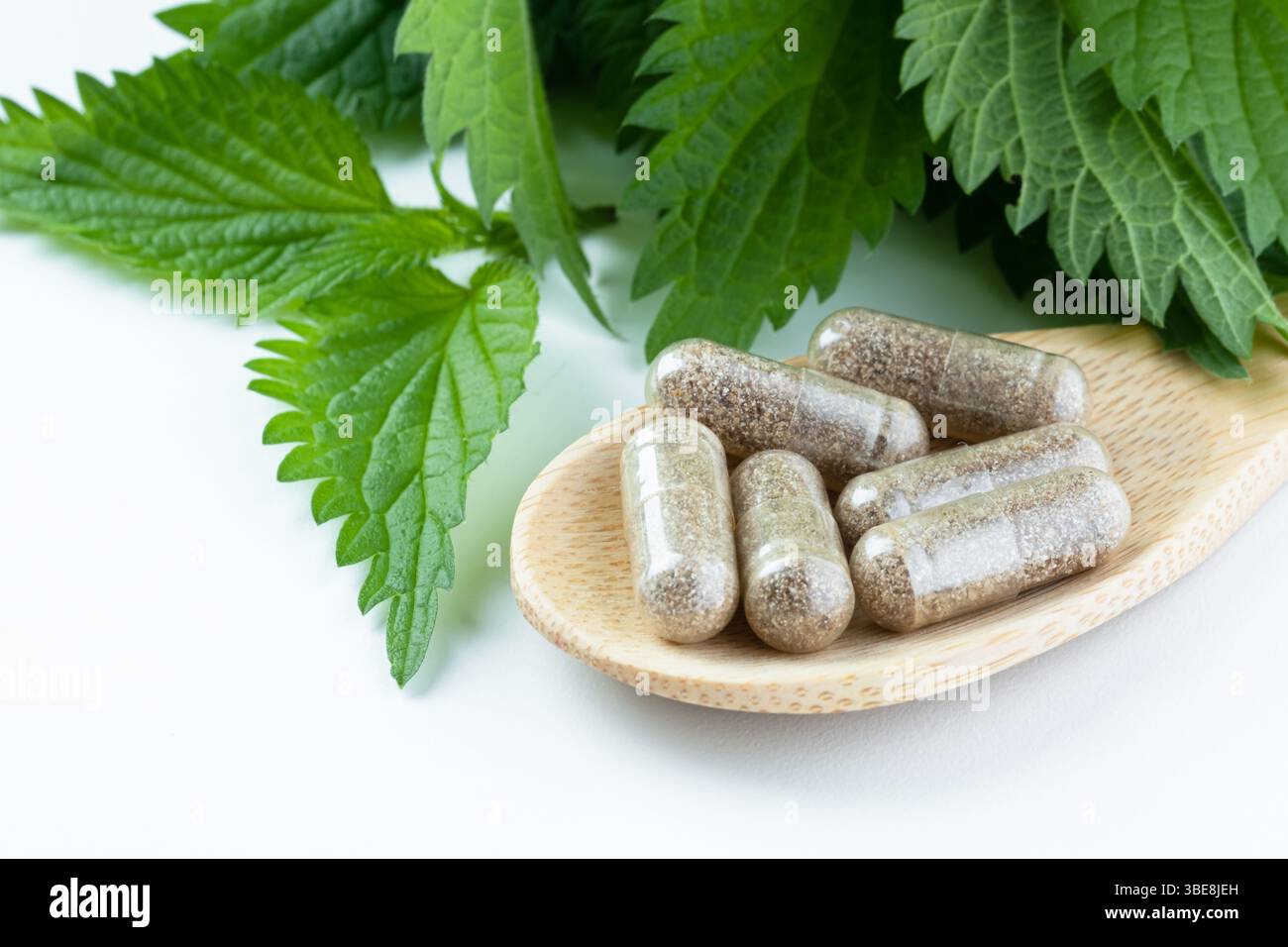 Integratori a base di erbe su un cucchiaio di legno con ortica su sfondo bianco. Medicina alternativa, concetto di tema sano e benessere. Foto Stock