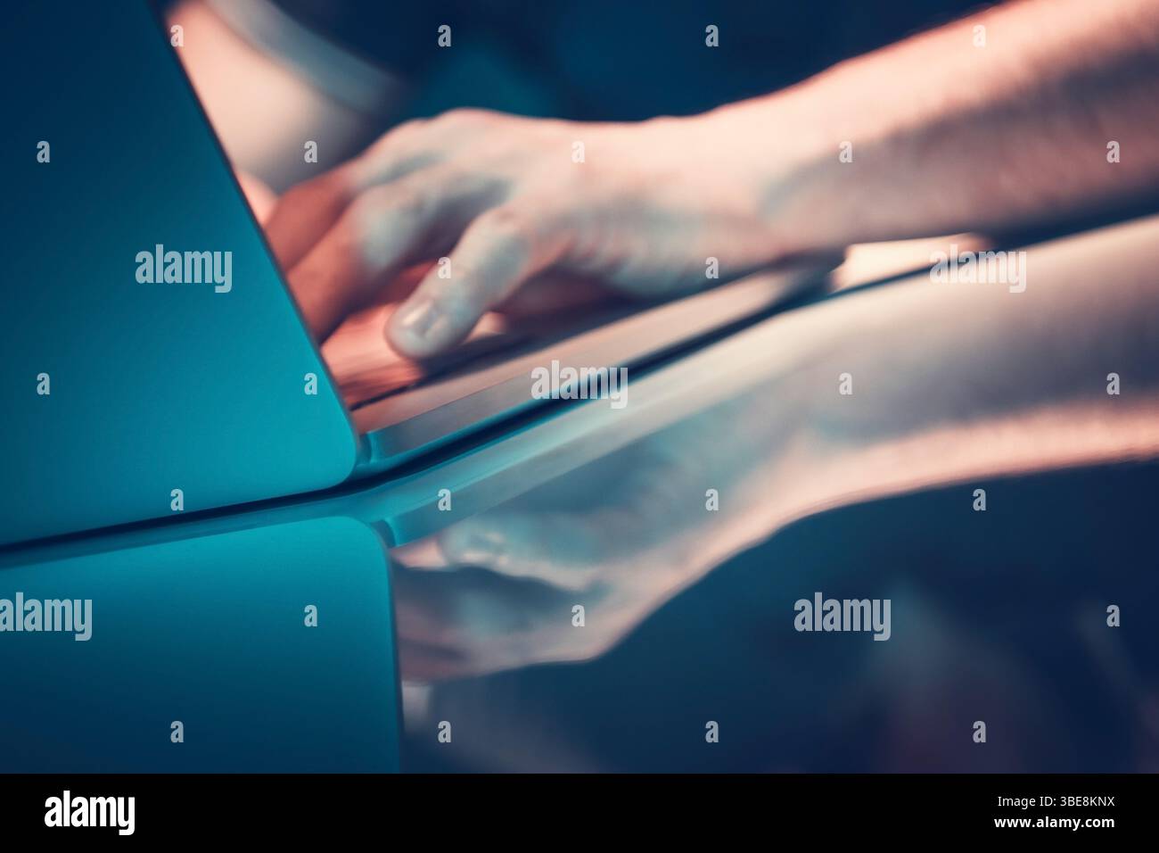 Le dita si spostano rapidamente sulla tastiera di un notebook mentre la luce riflessa migliora la superficie lucida sottostante. L'atmosfera è rilassata e concentrata. Foto Stock