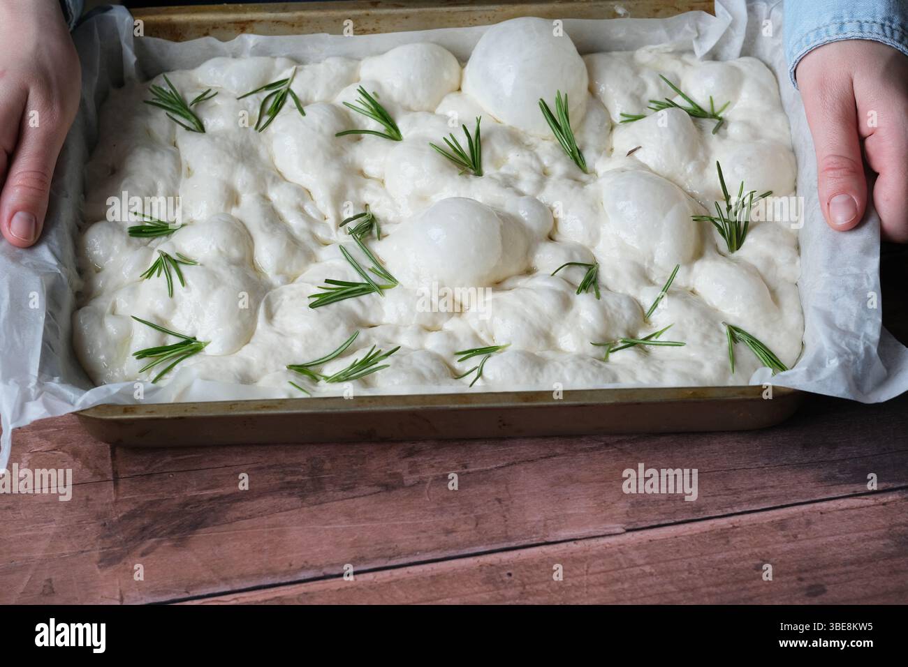 Mani di una persona irriconoscibile che tiene una muffa con soffice impasto di pane mentre si solleva in preparazione per la cottura in un ambiente accogliente Foto Stock