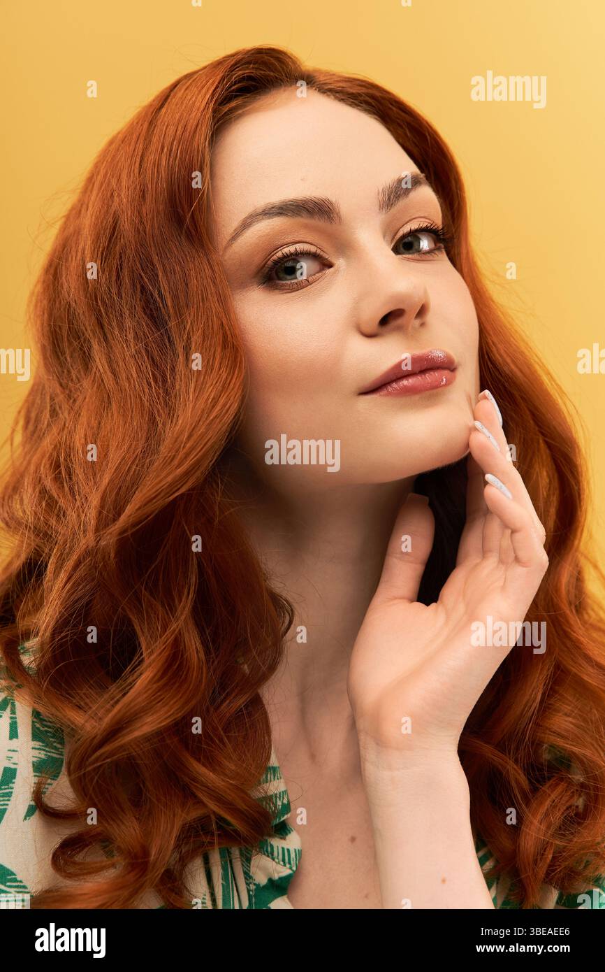 Una bella donna con ricci rossi che scorrono tocca delicatamente il viso, trasudando fiducia. Foto Stock