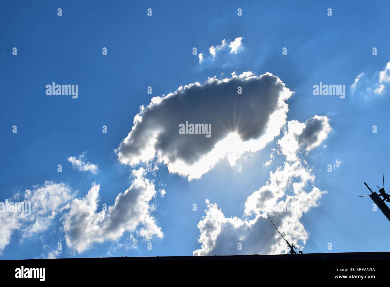 Le antenne si innalzano verso un cielo illuminato dai raggi del sole che si infrangono attraverso le nuvole sparse, evidenziando il contrasto tra le strutture create dall'uomo e la natura. Foto Stock