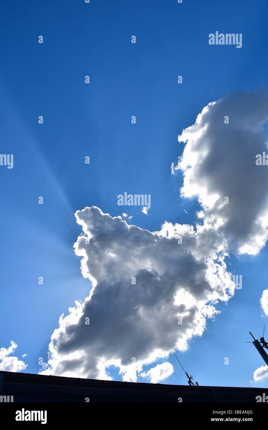 Un cielo sereno perforato dai raggi del sole, mentre le antenne sul tetto rimangono immobile, creando un tranquillo contrasto con il cielo spettacolare. Foto Stock