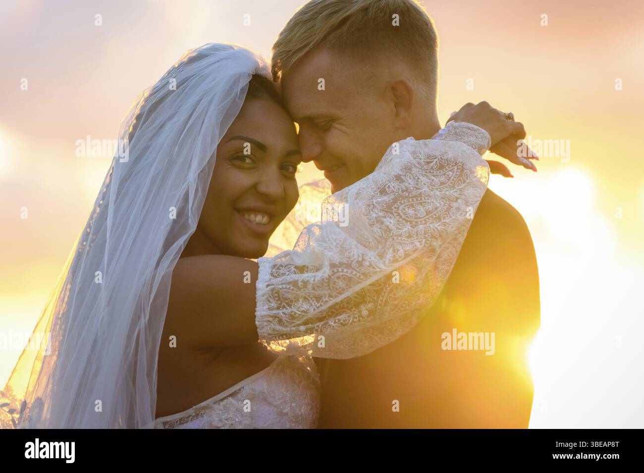 Felici sposi novelli che si abbracciano ai raggi del sole che tramonta Foto Stock