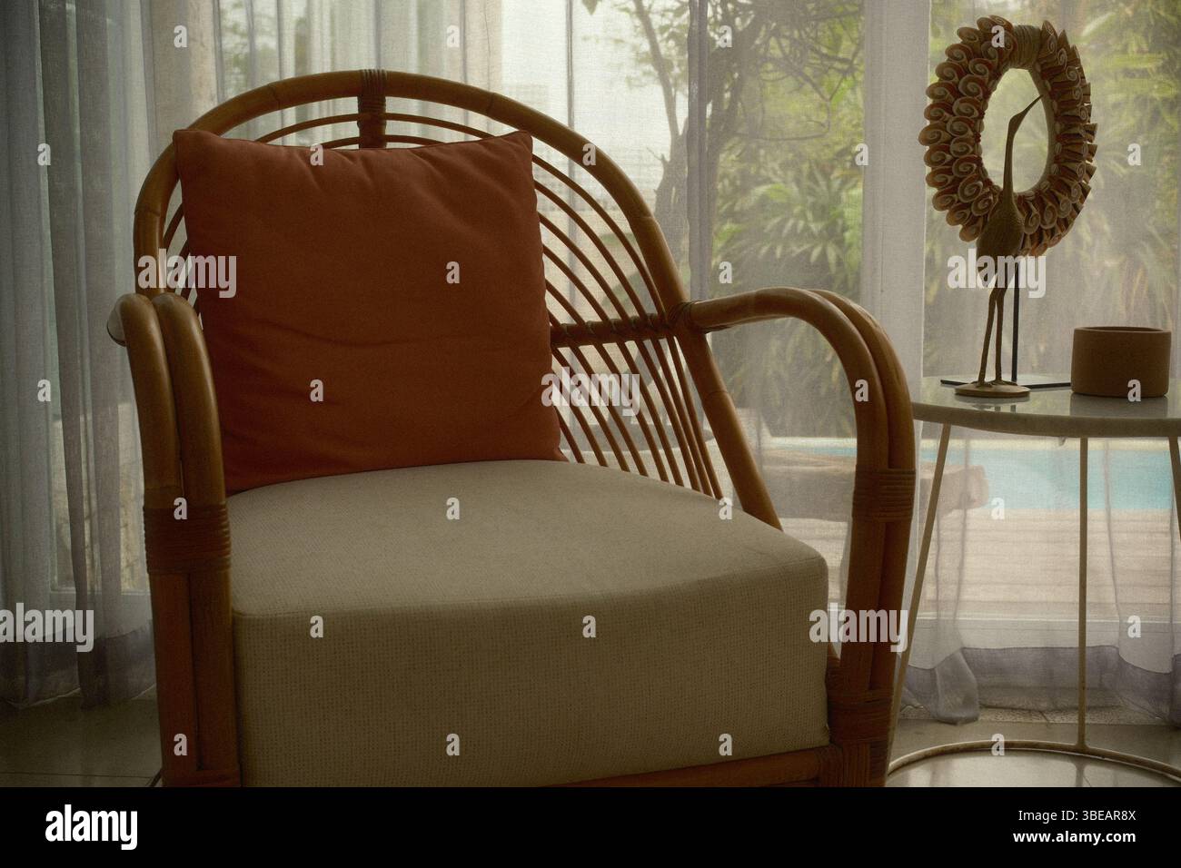 Angolo intimo con una poltrona in rattan, cuscino, un tavolino con piano in marmo bianco e una decorazione di sculture di uccelli a bordo piscina Foto Stock