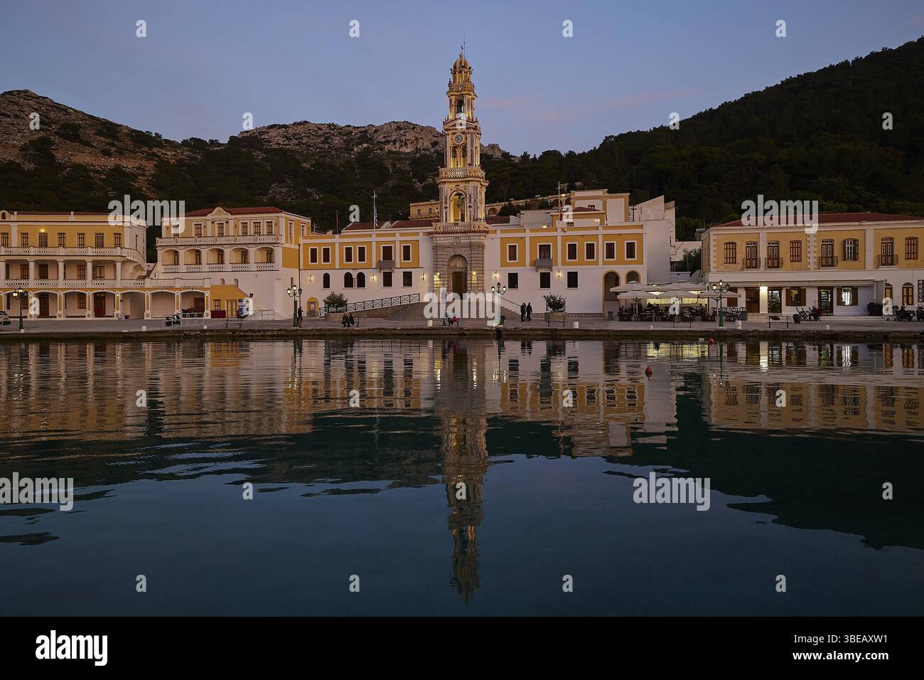 Vista notturna di una chiesa illuminata con riflessi nelle calme acque costiere, settimana Santa, Baia di Panormitis, Monastero di Panormitis, Symi, Dodecaneso, Foto Stock