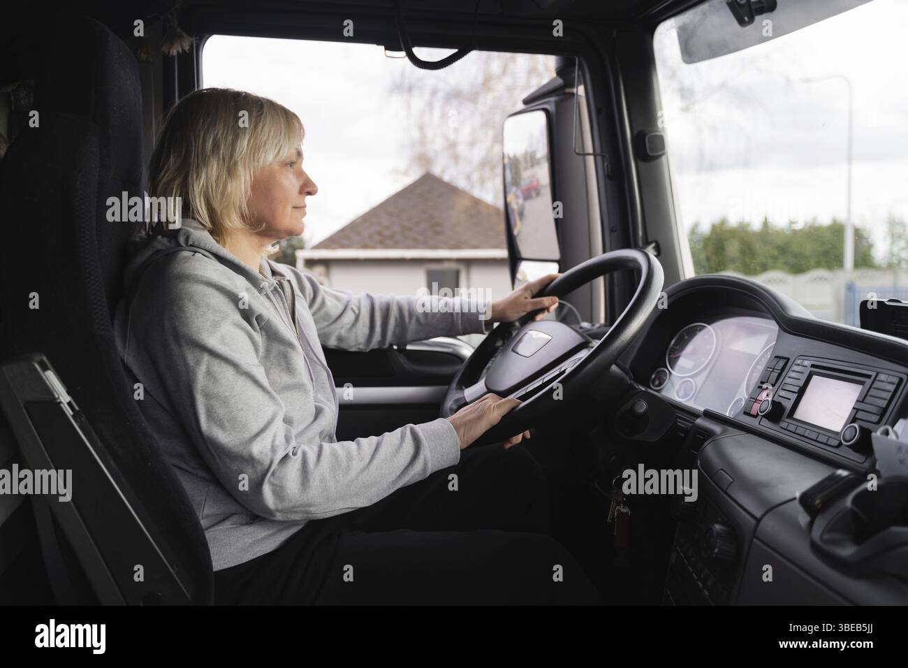 Donna caucasica di mezza età alla guida di un camion. camionista lavoratrice, professione nel settore dei trasporti . Foto Stock