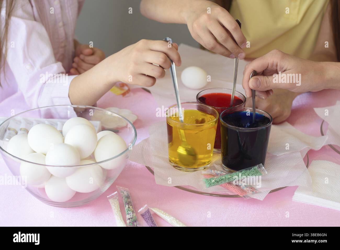 I bambini interferiscono con una soluzione con la colorazione degli alimenti nei bicchieri per dipingere le uova di Pasqua Foto Stock