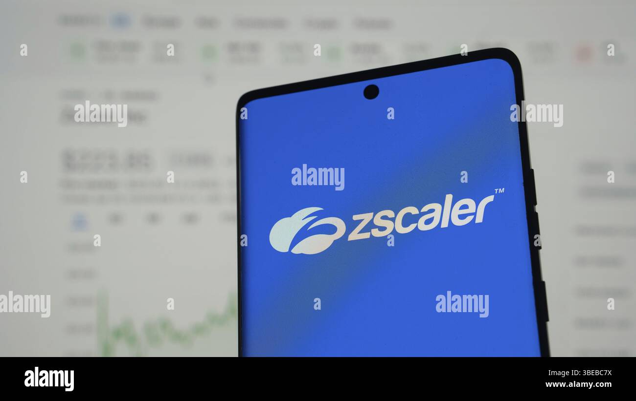 Logo Zscaler sullo schermo di un telefono con grafici finanziari su sfondo sfocato Foto Stock