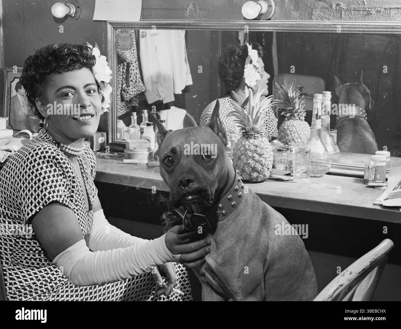 Billie Holiday e il suo cane Mister nello spogliatoio del Club Downbeat a febbraio 1947. Billie Holiday, nata Eleanora Fagan (New York, 7 aprile 1915 – New York, 17 luglio 1959), è stata una cantante statunitense di musica jazz e swing. Soprannominata "Lady Day" dalla sua amica e partner musicale, Lester Young, Holiday ha dato un contributo significativo alla musica jazz e al canto pop. Il suo stile vocale, fortemente influenzato dagli strumentisti jazz, ha ispirato un nuovo modo di manipolare il fraseggio e il tempo. Holiday era nota per le sue doti vocali e improvvisative Foto Stock
