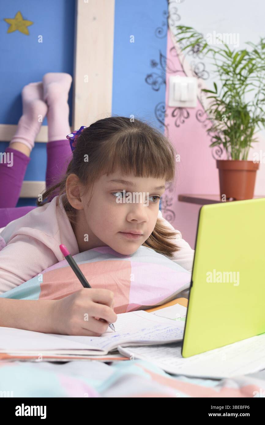 La scolaretta guarda i video tutorial in un tablet e si trova a letto Foto Stock