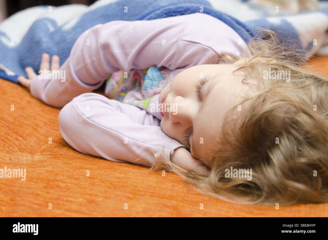 Una bambina di tre anni che dorme sul divano, mettendo una mano sotto la sua testa Foto Stock