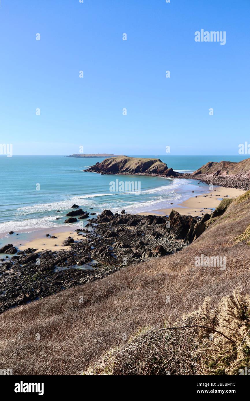 Scogliere aspre e spiaggia sabbiosa sulla costa del Pembrokeshire, Galles, sotto un cielo azzurro Foto Stock