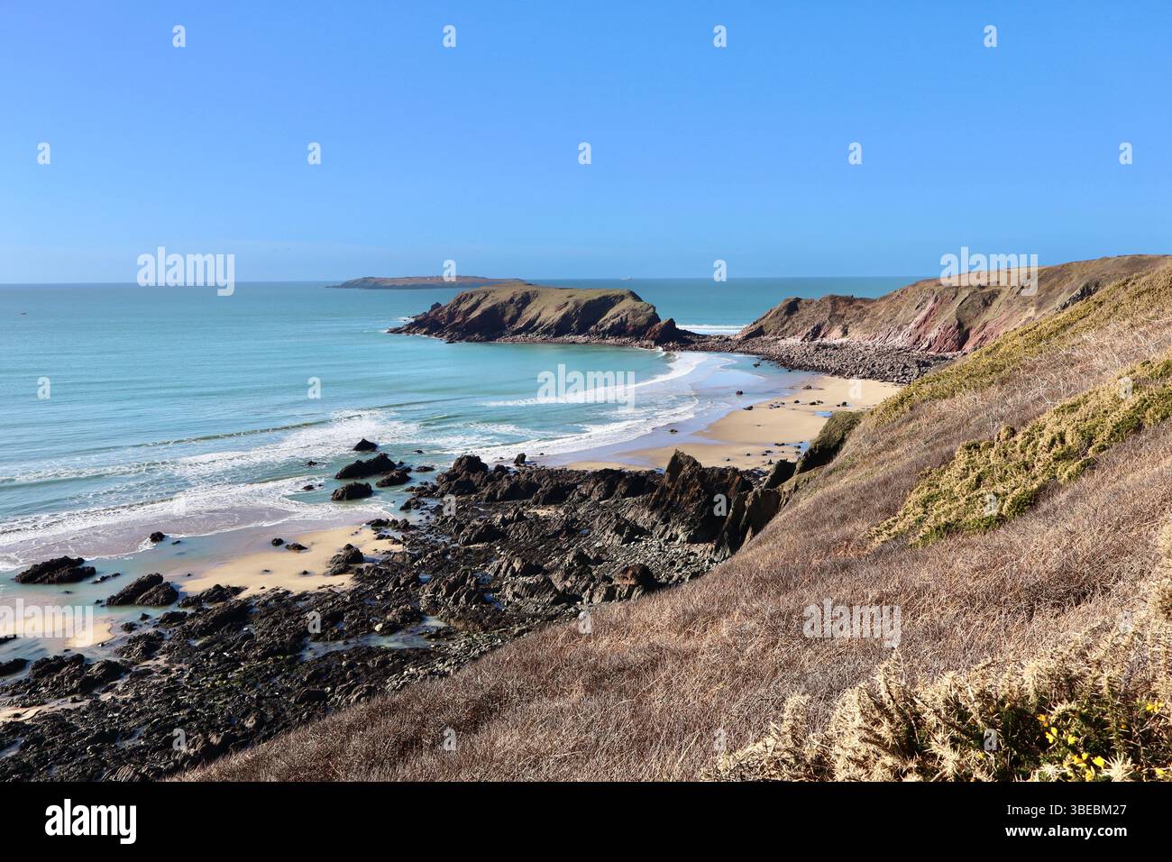 Scogliere aspre e spiaggia sabbiosa sulla costa del Pembrokeshire, Galles, sotto un cielo azzurro Foto Stock