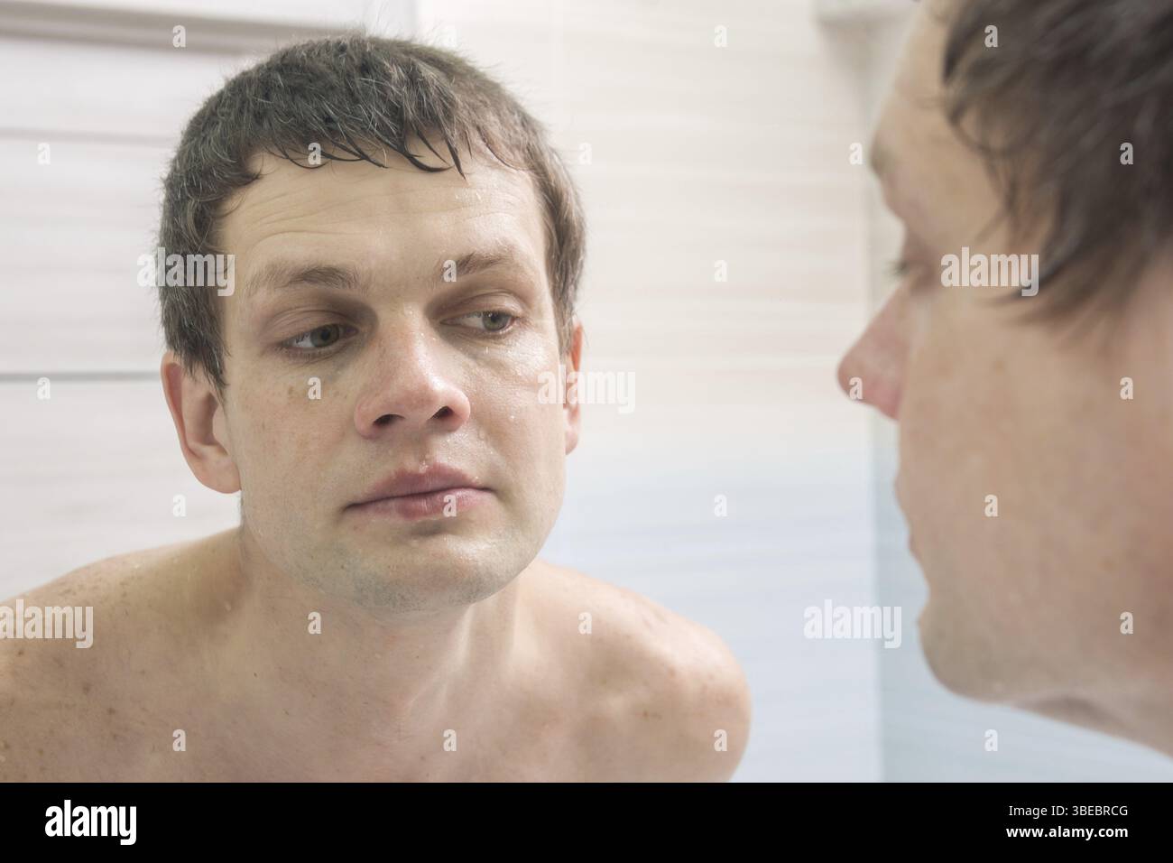 Una pulizia rasato giovane uomo guarda nello specchio Foto Stock