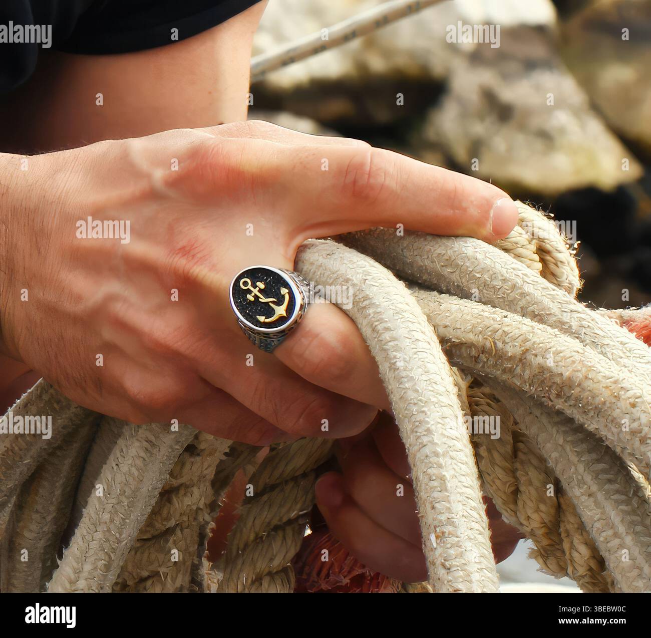 Marinaio che lavora con linee di ormeggio su un molo, indossa un anello con un ciondolo di ancora, simboleggia la tradizione marinara e il legame con la vita marittima Foto Stock