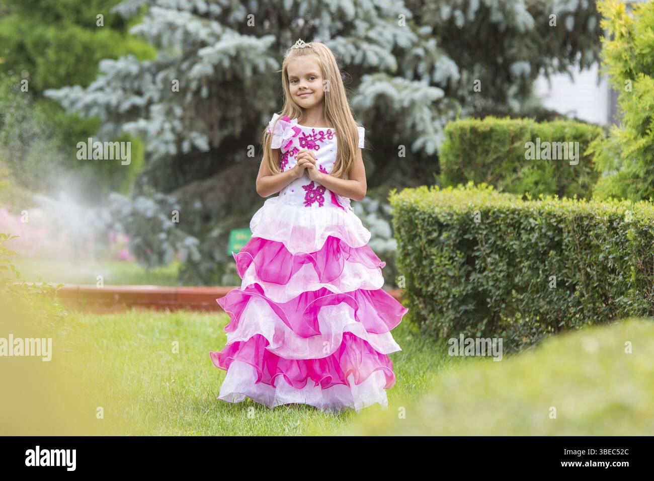 Sei felice anno vecchia ragazza in un lussureggiante sera abito rosa a piedi attraverso il giardino verde Foto Stock