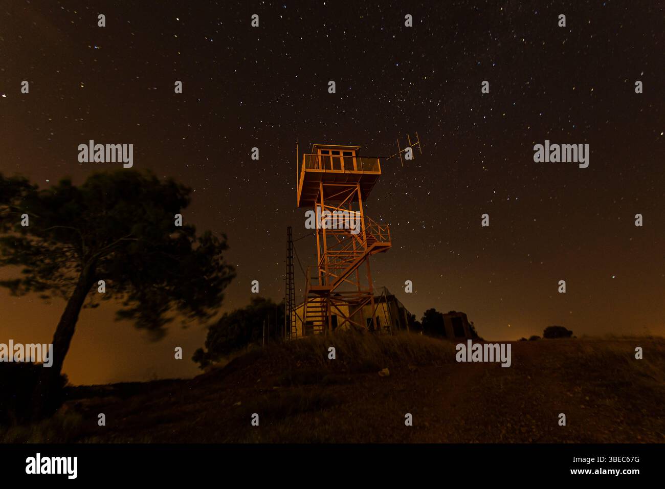 Una torre di avvistamento si erge su una collina mentre le stelle brillano in un cielo notturno limpido, offrendo un'atmosfera serena per gli astronomi. Foto Stock