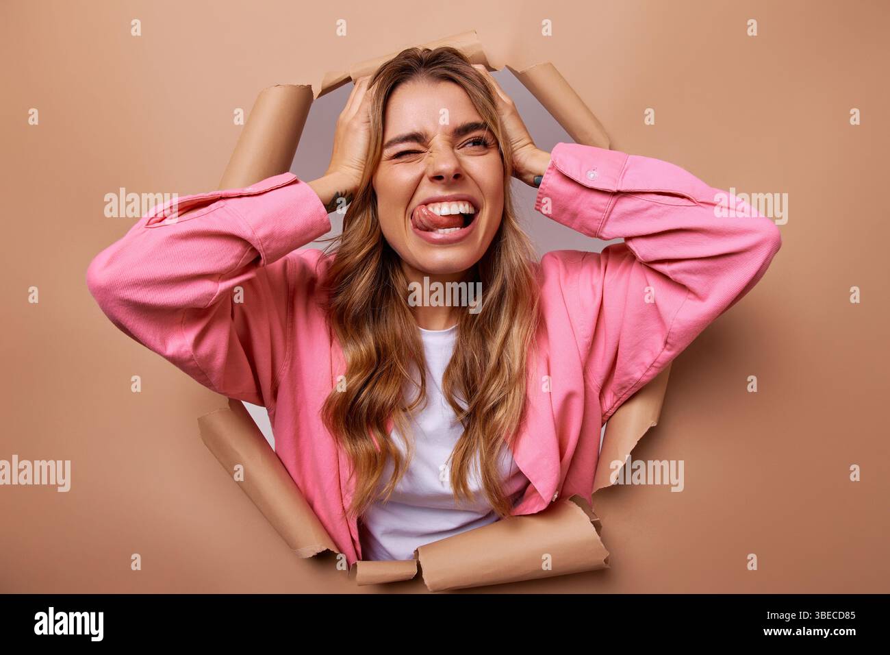 Una donna visibilmente frustrata irrompe attraverso un grande buco in un foglio di carta marrone, rivelando umoristicamente un'ampia gamma di emozioni ed espressioni, il tutto W Foto Stock
