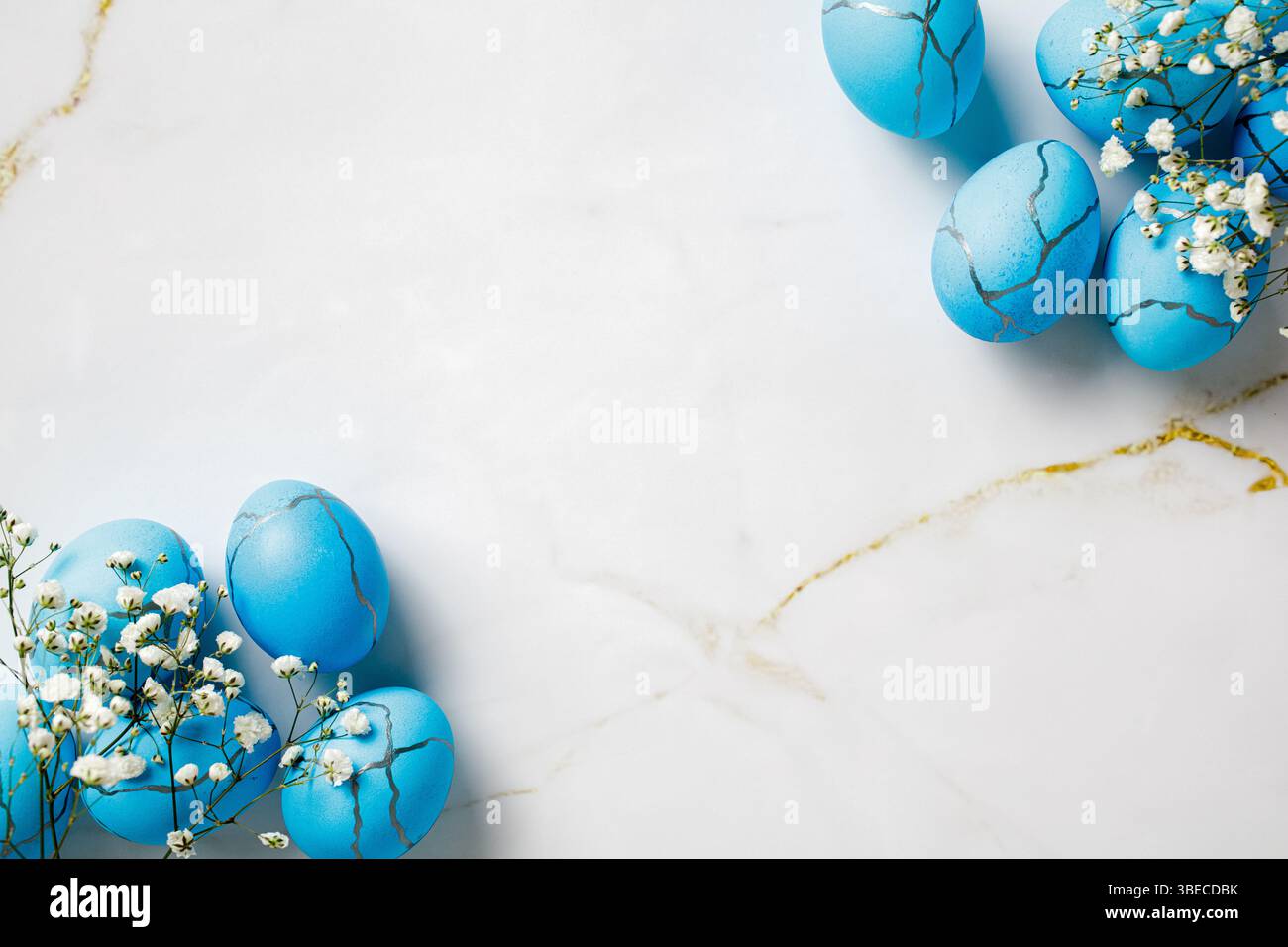 Cornice di uova di Pasqua blu e fiori bianchi su un tavolo di marmo Foto Stock