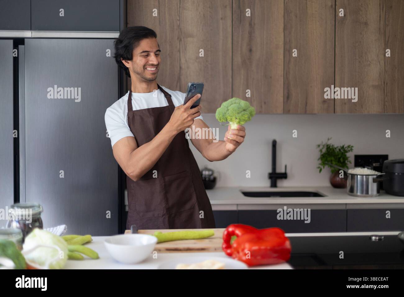 Lo chef fotografa i broccoli con il telefono in cucina, circondato da verdure fresche. Foto Stock