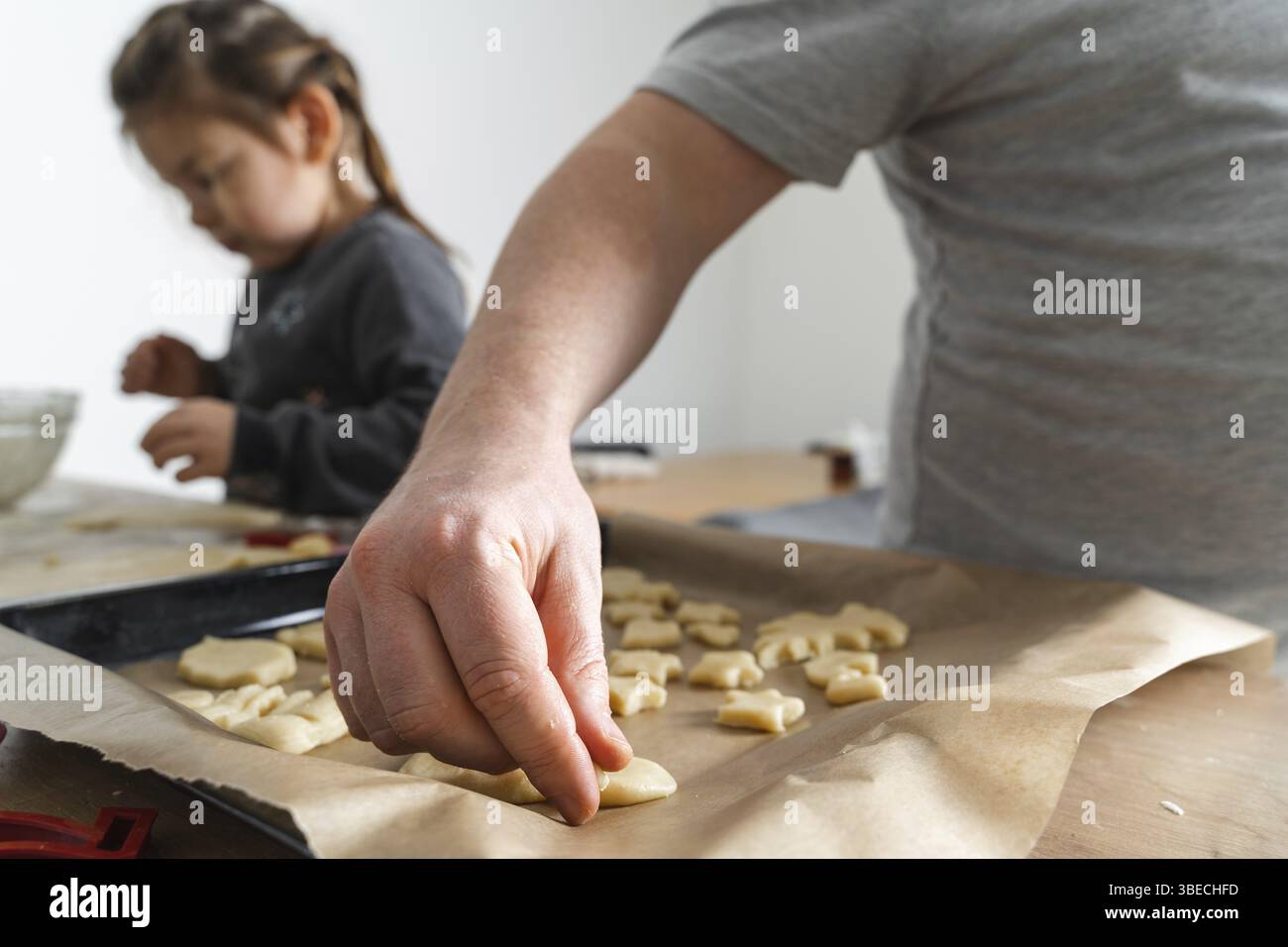 Vista ritagliata dell'uomo irriconoscibile e della figlia che fanno dolci con taglierine per biscotti sul pannello di lavorazione. Padre che mette i biscotti sulla teglia da forno Foto Stock