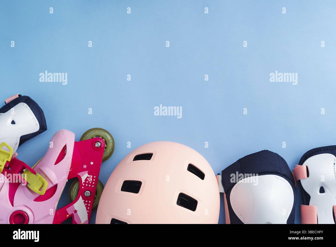 Vista dall'alto del set di attrezzature protettive per pattini a rotelle: Ginocchia, gomito, poggiapolsi e casco di colore rosa. Strato piatto su sfondo blu . Foto Stock