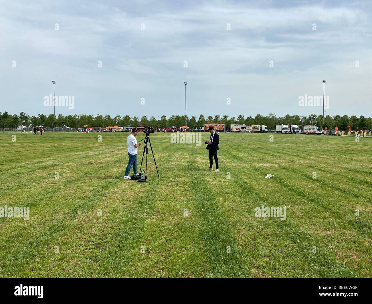 Ampio campo verde aperto con persone che preparano treppiedi e attrezzature durante un evento all'aperto in Turchia. - Immagine stock catturata con smartphone
