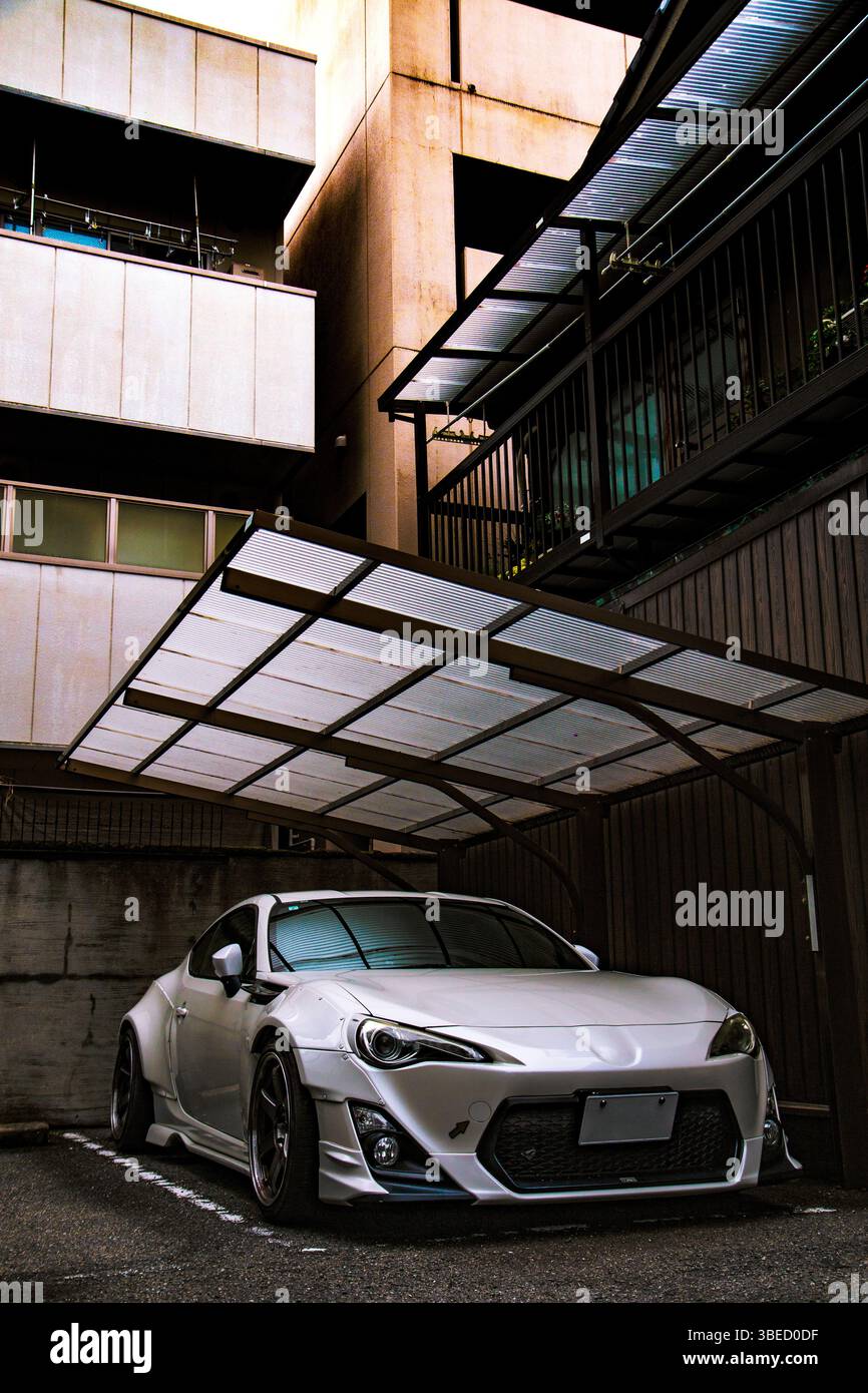 Toyota GT 86 parcheggiata sotto una tettoia urbana geometrica a Tokyo, Giappone, il suo elegante corpo in argento incorniciato da pareti in cemento e travi in metallo Foto Stock