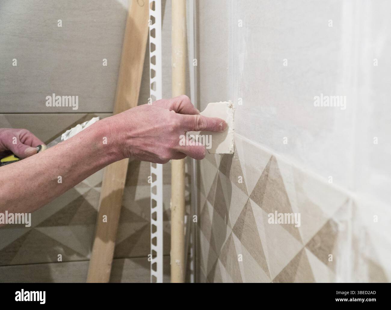 Lavoratore con una spatola in gomma riempire le giunzioni con una soluzione. Lavori di finitura, messa a fuoco sfocata. La tecnologia di posa delle piastrelle Foto Stock