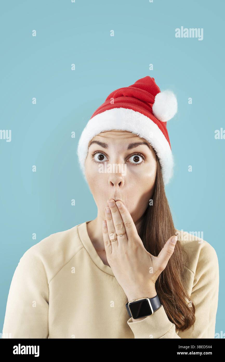 Donna caucasica con cappello di babbo natale ha sorpreso il ritratto. Sfondo blu. Foto Stock