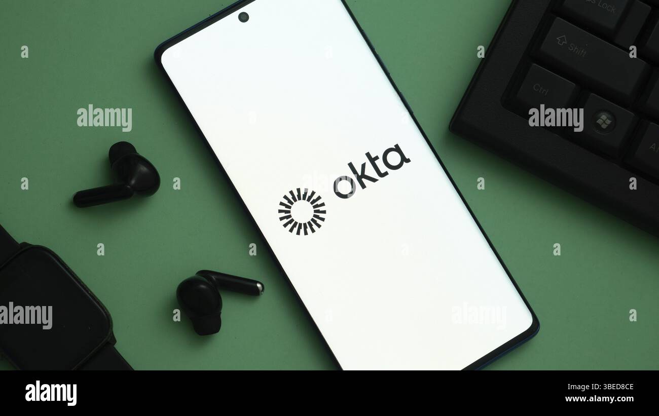 Smartphone con logo Okta circondato da gadget tecnologici sul verde Foto Stock